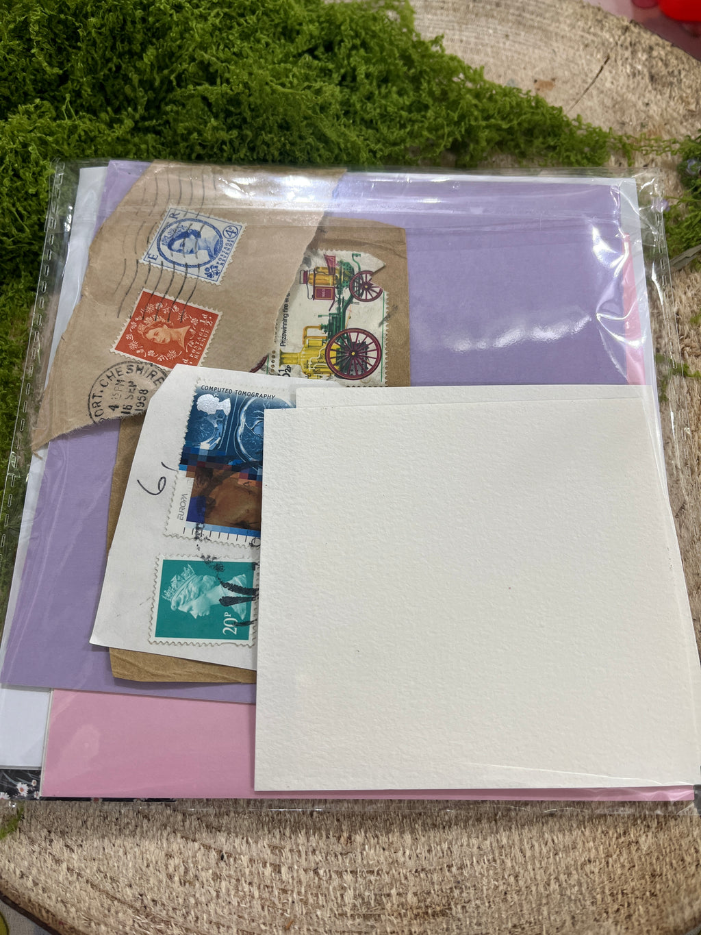 card making craft set, scrap card stickers & stamps with a purple and pink card, used stams a watercolour paper card on a wooden board with greenary