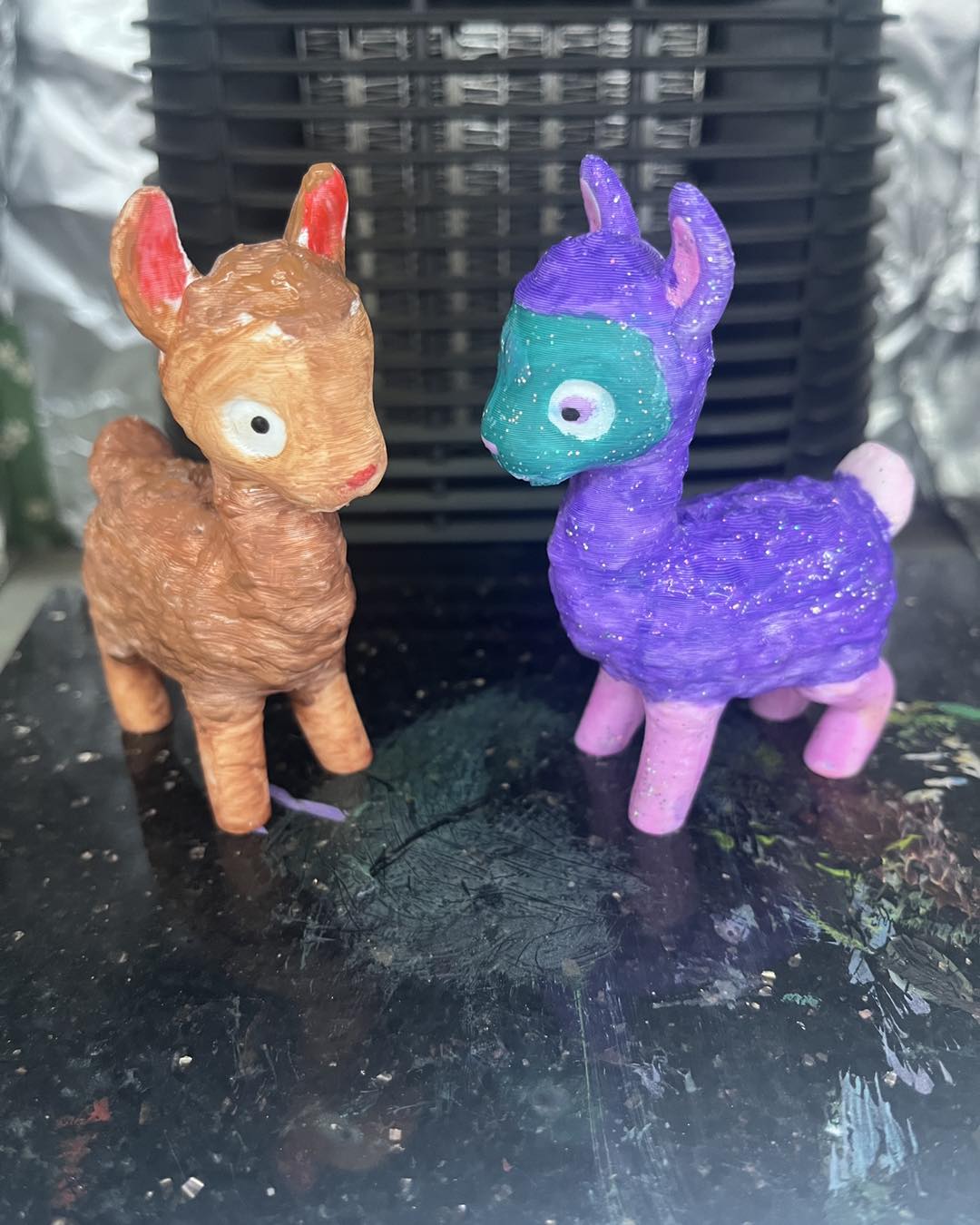 Two toy deer, one brown and one purple with teal face, on a dark surface. the wild fig and fern, things todo leicestershire