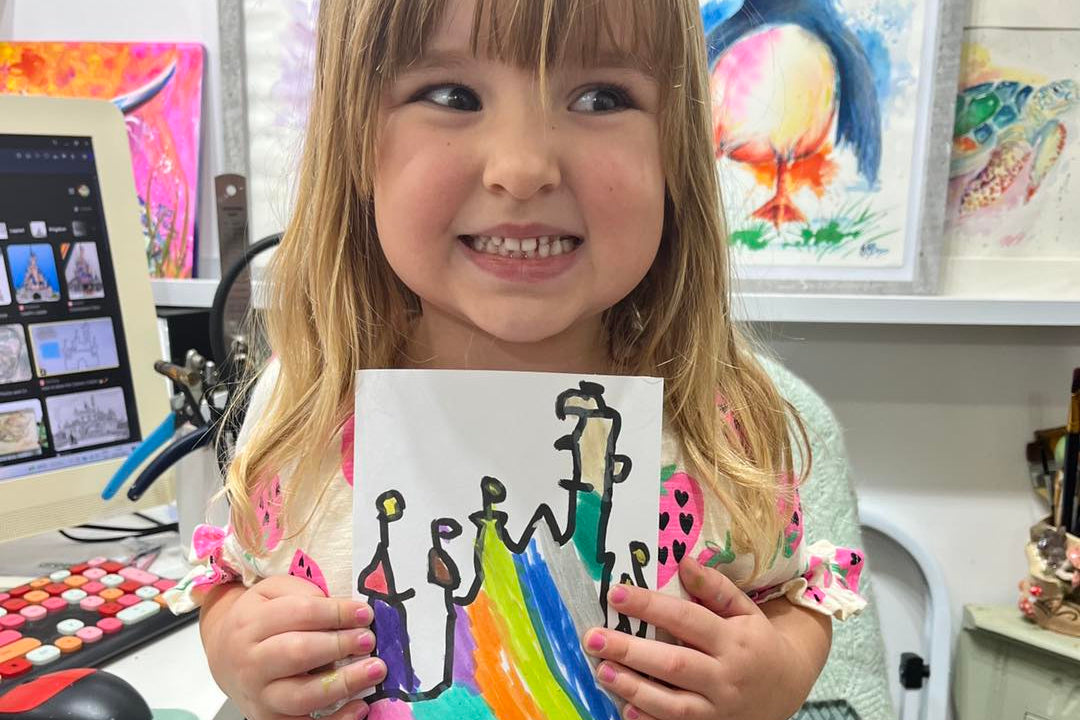 Young girl holding a drawing of people with a rainbow, in an art studio setting at the wild fig and fern leicestershire things todo.
